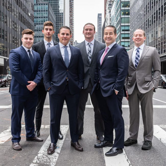Six men in business suits standing together in a city crosswalk.