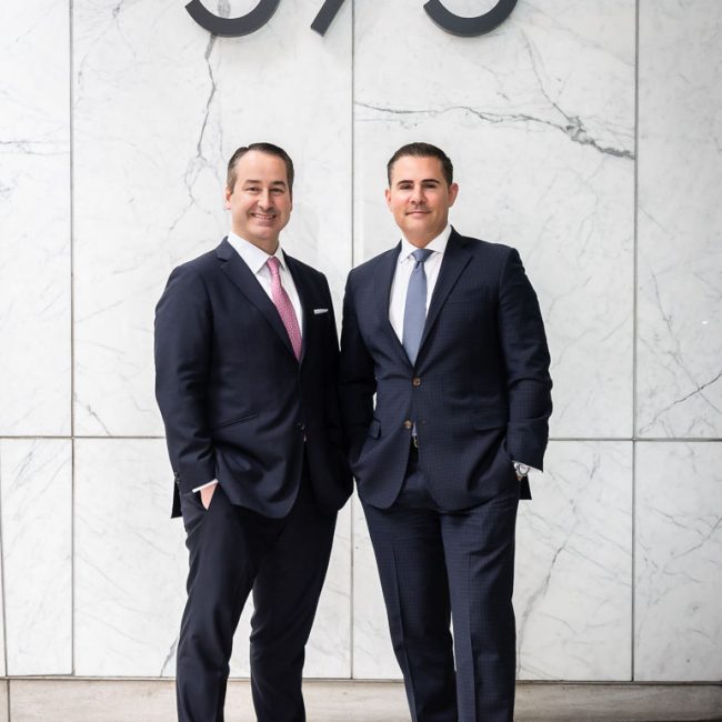 Two corporate executives standing together outside a marble office building in New York City.