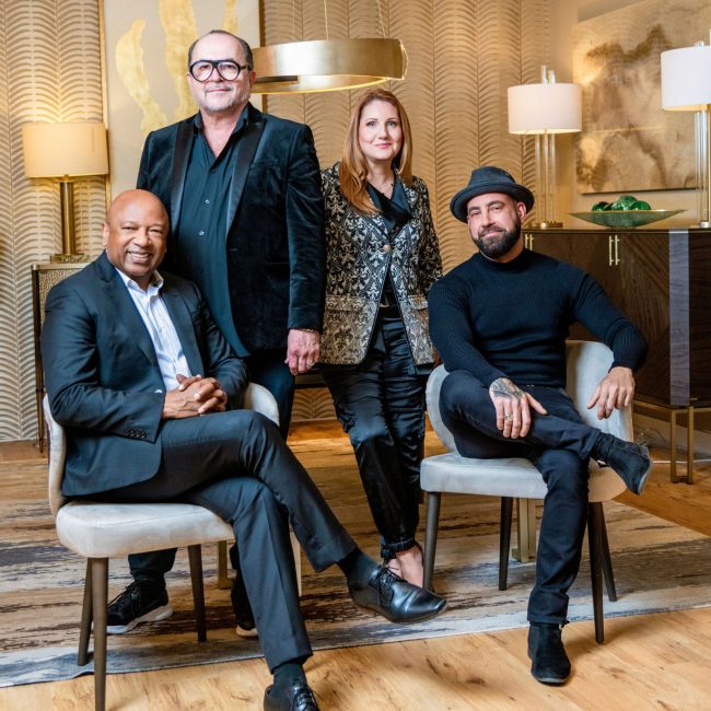 Portrait of a design team in black attire against a gold dining room backdrop, featured in a Boca Observer profile.