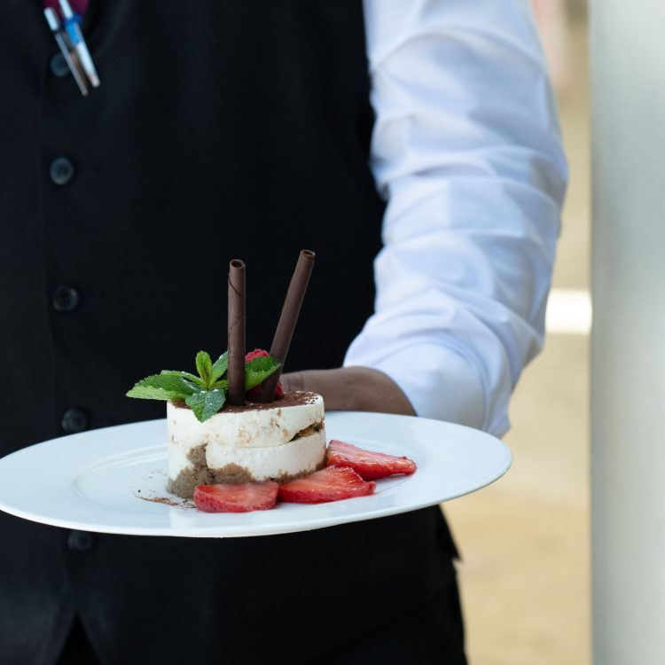Waiter serving a tiramisu dessert with strawberries and mint