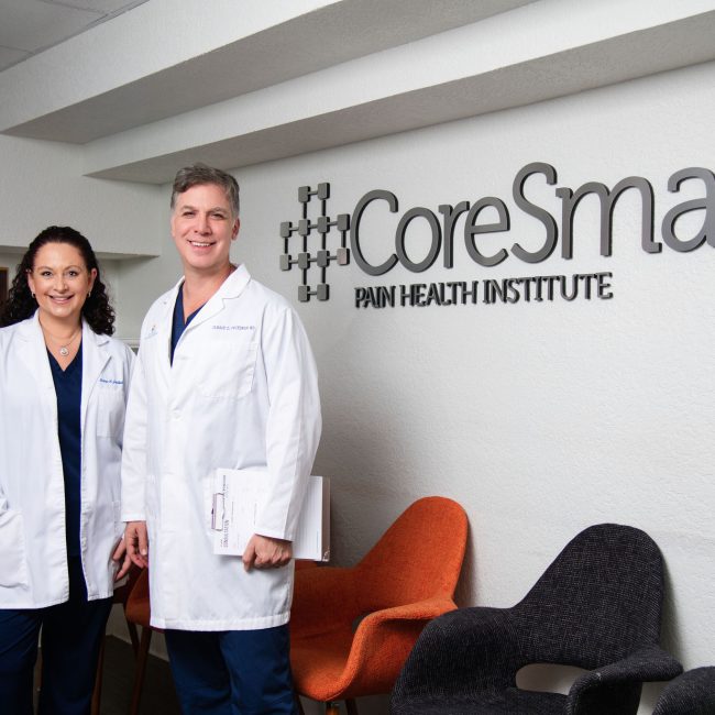 A man and woman in white medical coats standing in front of the CoreSmart Pain Health Institute sign.
