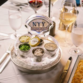 Caviar service on ice at NYY Steak, with condiments, wine glasses, and blinis on a table setting.