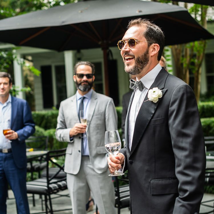 Groom in tuxedo smiles with champagne at outdoor wedding reception in Boca Raton.