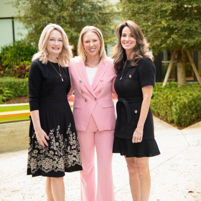Three women in business attire standing together outdoors in a courtyard.