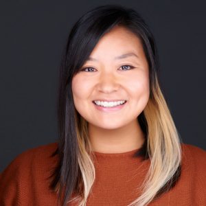 Headshot of a smiling woman with dark hair, wearing a rust-colored sweater.