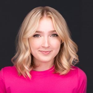 Headshot of a woman with blonde wavy hair, wearing a pink top.